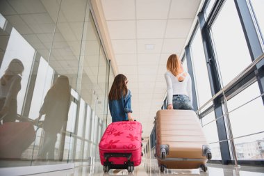 Mutlu genç anne ve kızı havaalanı terminalinde bir bavul taşırken yürüyorlar. Yüksek mevsim ve tatil konsepti. Rahatlayın ve yaşam tarzları