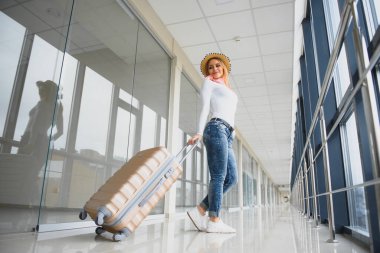 Gündelik giysiler giyen genç bir kadın havaalanında poz veriyor, çanta tutuyor ve kalkış pistinde bagajın yanında bekliyor..