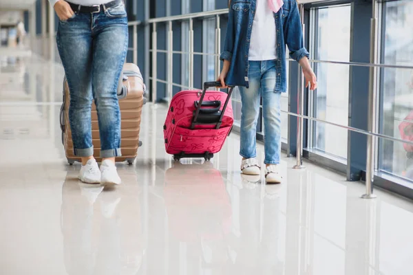 Mutlu genç anne ve kızı havaalanı terminalinde bir bavul taşırken yürüyorlar. Yüksek mevsim ve tatil konsepti. Rahatlayın ve yaşam tarzları