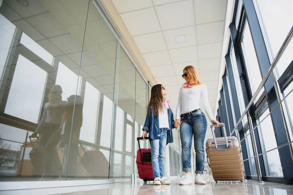 Beautiful mother and her stylish cute daughter walk together and pull a pink suitcase at airport. High season and vacation concept. Relax and lifestyles