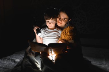 Mutlu bir aile. Hikaye zamanı. Mutlu, mutlu bir anne ve oğul uyumadan önce kitap okuyor ve el feneri kullanıyor..