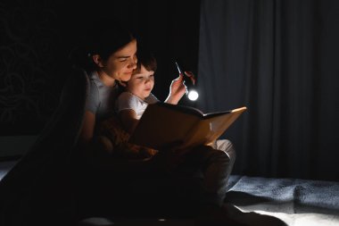 Mutlu bir aile. Hikaye zamanı. Mutlu, mutlu bir anne ve oğul uyumadan önce kitap okuyor ve el feneri kullanıyor..