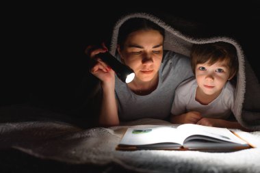 Mutlu bir aile. Hikaye zamanı. Mutlu, mutlu bir anne ve oğul uyumadan önce kitap okuyor ve el feneri kullanıyor..