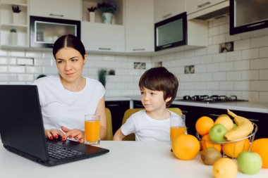 Mutfakta tablet bilgisayar kullanan bir aile, oğlu olan bir anne mutlu bir gülümseme, modern bir mutfak portakal suyu.