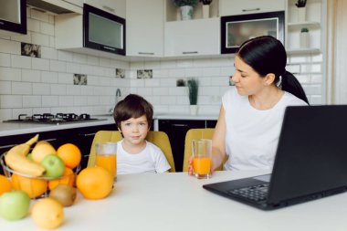 Mutfakta tablet bilgisayar kullanan bir aile, oğlu olan bir anne mutlu bir gülümseme, modern bir mutfak portakal suyu.