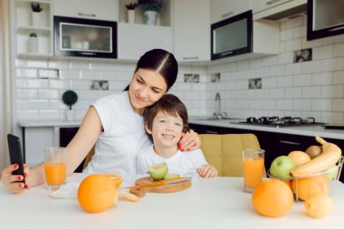 Küçük çocuk ve anne meyvelerle oynuyorlar ve oynuyorlar. Tişört giyiyorlar.