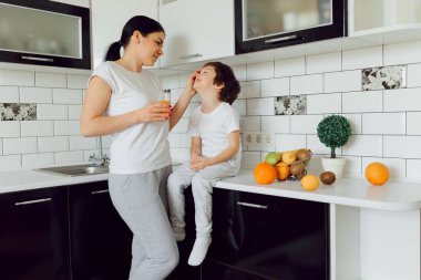 Küçük çocuk ve anne meyvelerle oynuyorlar ve oynuyorlar. Tişört giyiyorlar.