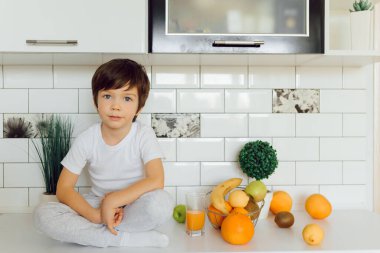 Mutfakta bir kase taze meyve taşıyan küçük bir çocuk.