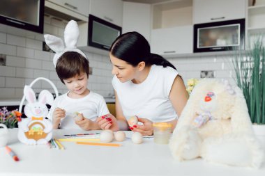 Mutlu bir aile. Anne ve oğlu yumurta boyuyor. Aile mutfakta oturuyor. Paskalya için hazırlanılıyor