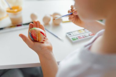 Paskalya yumurtalarını beyaz arka planda tutan bebek elleri. Çocuk yumurta boyuyor. Mutlu kız Paskalya için hazırlanıyor.