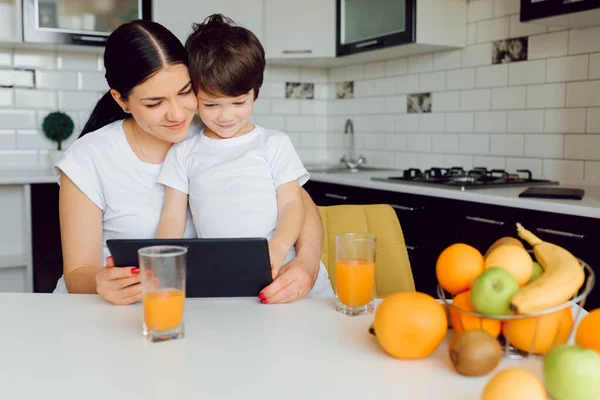 Family using a tablet pc in kitchen, mother with son happy smile, modern kitchen orange juice