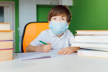 CoVid-19 karantinası sırasında koruyucu maskeyle evde ders çalışan yorgun bir çocuk bilgisayarla uzaktan öğrenme, okul için ödev yapan bir çocuk. Öğrenci evde kaldı..