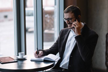Bir kafede yakışıklı bir işadamı telefonda konuşuyor.