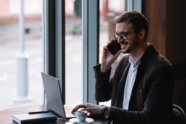 Genç başarılı iş adamı kafede otururken dizüstü bilgisayarda çalışıyor..