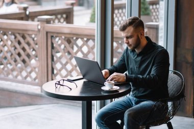 Genç başarılı iş adamı kafede otururken dizüstü bilgisayarda çalışıyor..