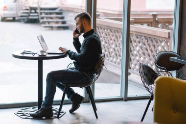 Genç başarılı iş adamı kafede otururken dizüstü bilgisayarda çalışıyor..