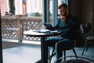 Yakışıklı iş adamı dijital tablet kullanıyor ve şehir merkezindeki kafede otururken kahve içiyor.