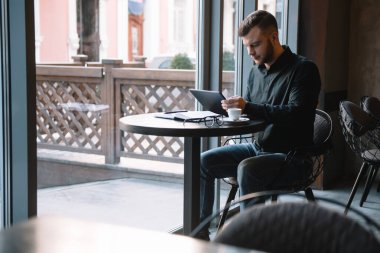 Yakışıklı iş adamı dijital tablet kullanıyor ve şehir merkezindeki kafede otururken kahve içiyor.