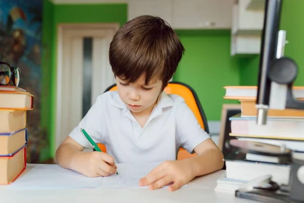 The boy is studying at home during CoVid-19 quarantine, distance learning online with a laptop, the child is doing homework for school. The schoolboy stayed at home.