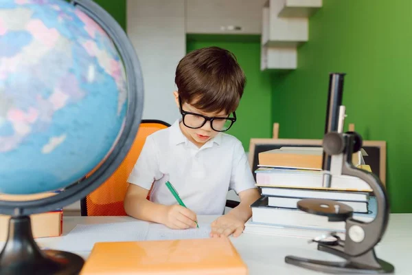 The boy is studying at home during CoVid-19 quarantine, distance learning online with a laptop, the child is doing homework for school. The schoolboy stayed at home.