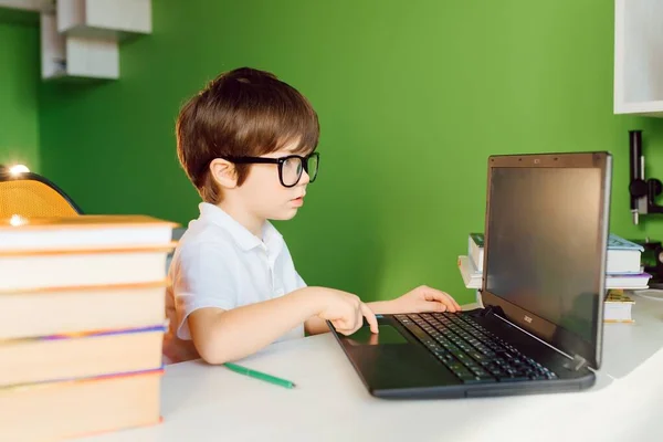 The boy is studying at home during CoVid-19 quarantine, distance learning online with a laptop, the child is doing homework for school. The schoolboy stayed at home.