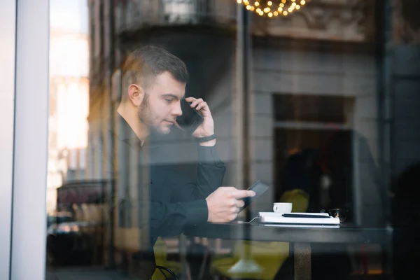 Young businessman talking on mobile phone while working on laptop in cafe