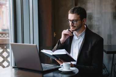 Genç başarılı iş adamı kafede otururken dizüstü bilgisayarda çalışıyor..