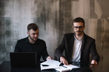 Bir bilgisayarın arkasında çalışırken kameraya gülümseyen iki iş adamı.