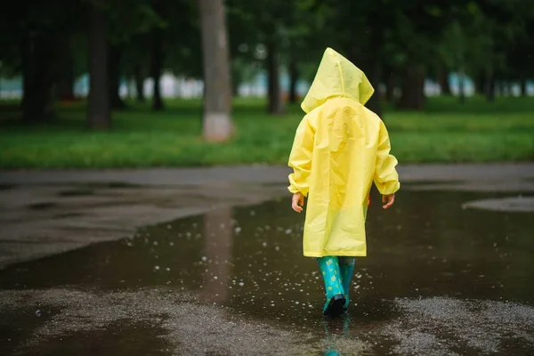 雨の夏の公園で遊んでいる男の子 雨の中で水たまりや泥の中でジャンプ傘 防水コートやブーツと子供 子供は夏の雨の中を歩くどんな天気でも屋外の楽しみ 幸せな子供時代 — ストック写真