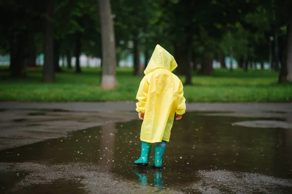 雨の夏の公園で遊んでいる男の子 雨の中で水たまりや泥の中でジャンプ傘 防水コートやブーツと子供 子供は夏の雨の中を歩くどんな天気でも屋外の楽しみ 幸せな子供時代 — ストック写真