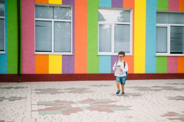 Okula dönelim. Gözlüklü mutlu çocuk ilk kez okula gidiyor. Sırt çantası ve kitabı olan bir çocuk. Dersler başlıyor. Sonbaharın ilk günü.