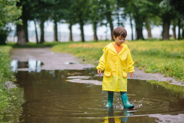 雨の夏の公園で遊んでいる男の子 雨の中で水たまりや泥の中でジャンプ傘 防水コートやブーツと子供 子供は夏の雨の中を歩くどんな天気でも屋外の楽しみ 幸せな子供時代 — ストック写真