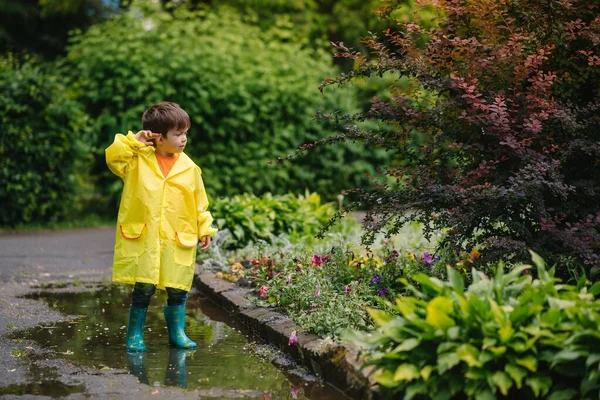 雨の夏の公園で遊んでいる男の子 雨の中で水たまりや泥の中でジャンプ傘 防水コートやブーツと子供 子供は夏の雨の中を歩くどんな天気でも屋外の楽しみ 幸せな子供時代 — ストック写真