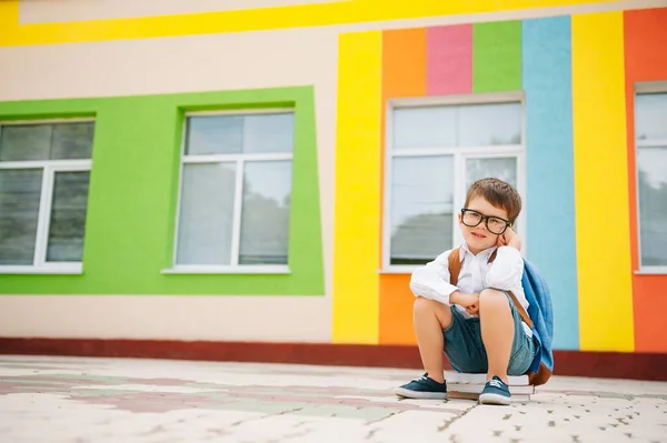 学校の外で悲しい少年 現代の学校の近くに本を持つ悲しい小学生 学校のコンセプト 学校に戻る — ストック写真