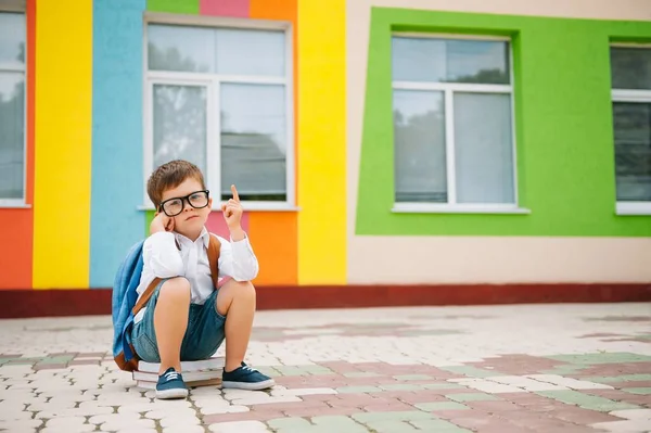 Sad little boy outside of school. Sad schoolboy with books near a modern school. School concept. Back to school.