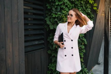 Ofisin yanında gururla dururken elinde dijital tablet ve klasör tutan başarılı bir iş kadınının portresi