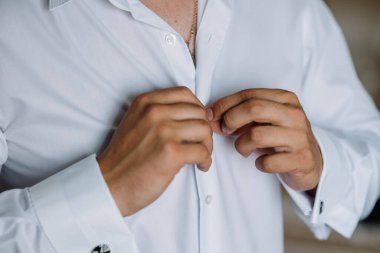 Beyaz gömleğin arka planında erkek elleri kol düğmeleri ve saatlerle kol gömleği, yakın plan çekimleri.