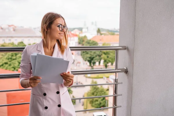 successful business woman with financial documents standing near a large window in a modern office