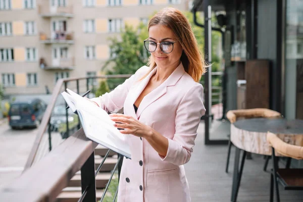 successful business woman with financial documents standing near a large window in a modern office