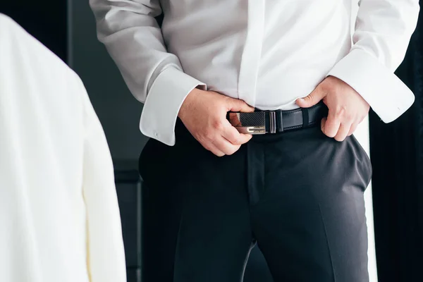 一个穿黑裤子和白衬衫的男人扣上了一条棕色皮裤腰带 — 图库照片