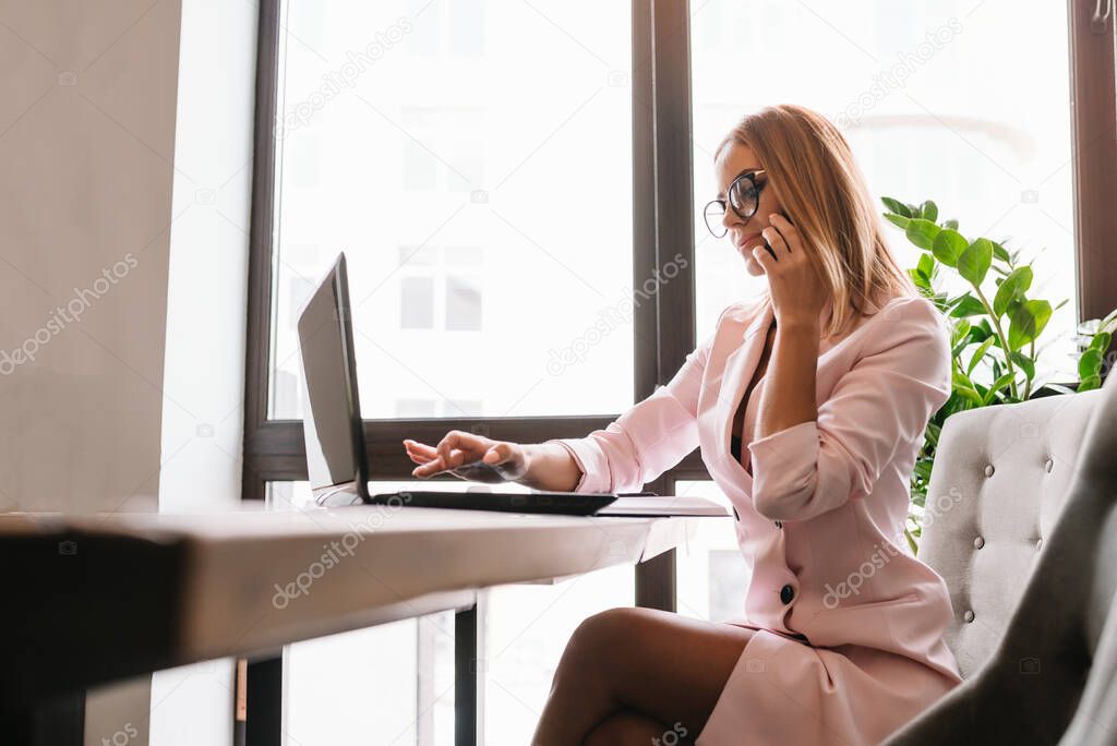Portrait of smiling pretty young business woman in glasses sitting on workplace