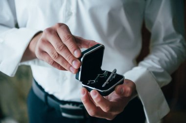 Beyaz gömleğin arka planında erkek elleri kol düğmeleri ve saatlerle kol gömleği, yakın plan çekimleri.