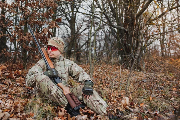 座っている間に銃を持つ男性ハンターは森を目指しています 成功した狩り 経験豊富なハンターの概念 秋のシーズンを狩り ハンターにはライフルと狩猟用の制服がある — ストック写真