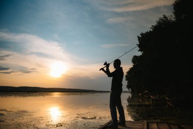Nehirde gün batımında balıkçı. Nehirde günbatımı olan güzel bir yaz manzarası. Balık tutmaya. Gün batımında dönüyor. Bir balıkçının silueti.