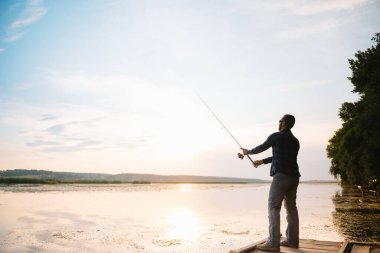 Genç adam puslu gündoğumunda balık tutuyor.