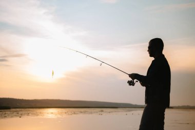 Genç adam puslu gündoğumunda balık tutuyor.