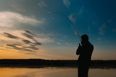Nehirde gün batımında balıkçı. Nehirde günbatımı olan güzel bir yaz manzarası. Balık tutmaya. Gün batımında dönüyor. Bir balıkçının silueti.