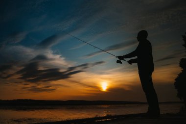 Nehirde gün batımında balıkçı. Nehirde günbatımı olan güzel bir yaz manzarası. Balık tutmaya. Gün batımında dönüyor. Bir balıkçının silueti.