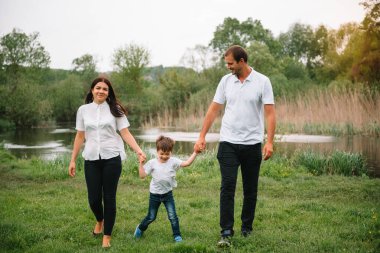 Mutlu aile: anne baba ve çocuk gün batımında doğada. Anne, baba ve çocuk gülüyor, sarılıyor, dışarıda doğanın tadını çıkarıyor. Güneşli bir gün, iyi bir ruh hali. Mutlu aile kavramı