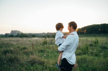 Yakışıklı baba ve küçük tatlı oğlu yeşil çimenlikte eğleniyor ve oynuyorlar. Mutlu aile kavramı. Aile hayatı olan güzel doğa manzarası. Aile birlikte dinleniyor. Babalar Günü
